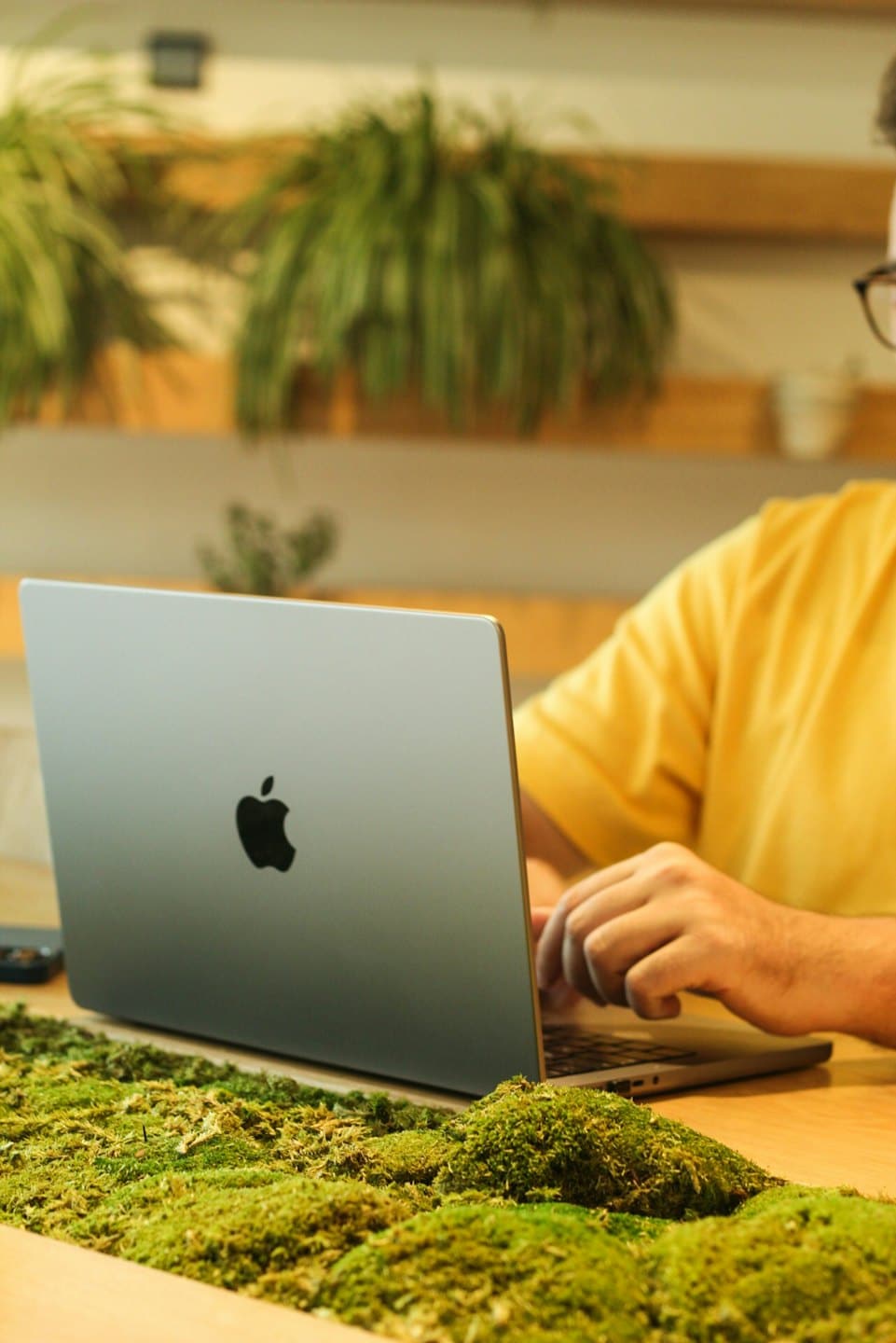 Person typing on a silver laptop at a wooden desk.