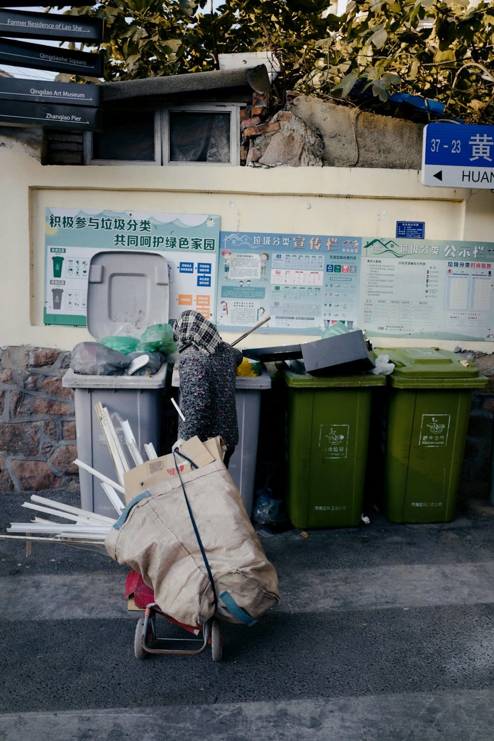 Person sorting recycling bins by a poster-covered wall.